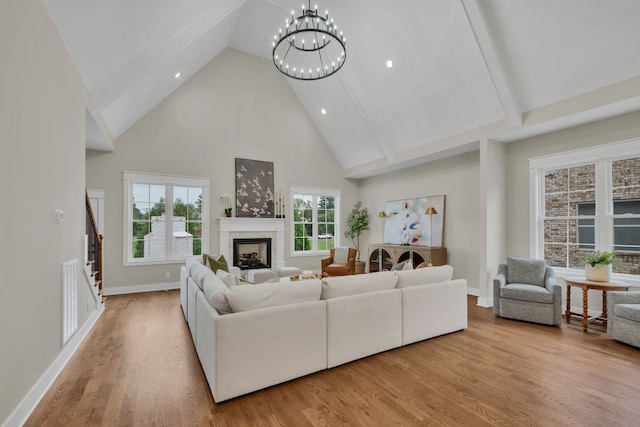 living room featuring a premium fireplace, beam ceiling, high vaulted ceiling, a chandelier, and light wood-type flooring