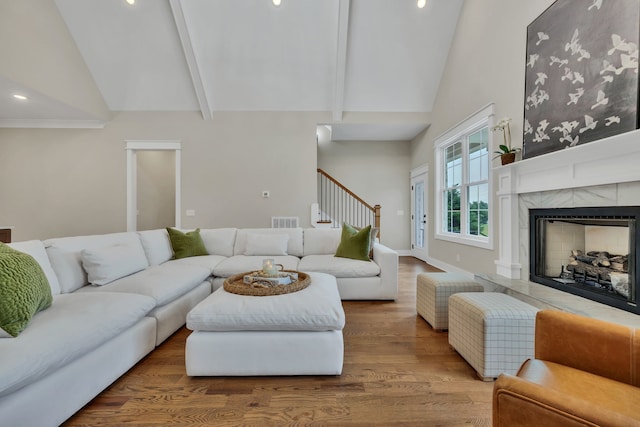 living room featuring high vaulted ceiling, hardwood / wood-style flooring, beam ceiling, and a tile fireplace