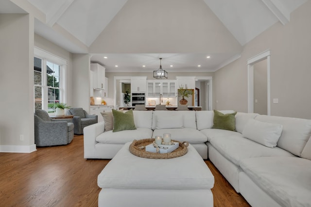 living room featuring high vaulted ceiling, beamed ceiling, wood-type flooring, and a chandelier