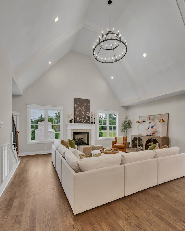 living room with high vaulted ceiling, a tiled fireplace, wood-type flooring, and a chandelier