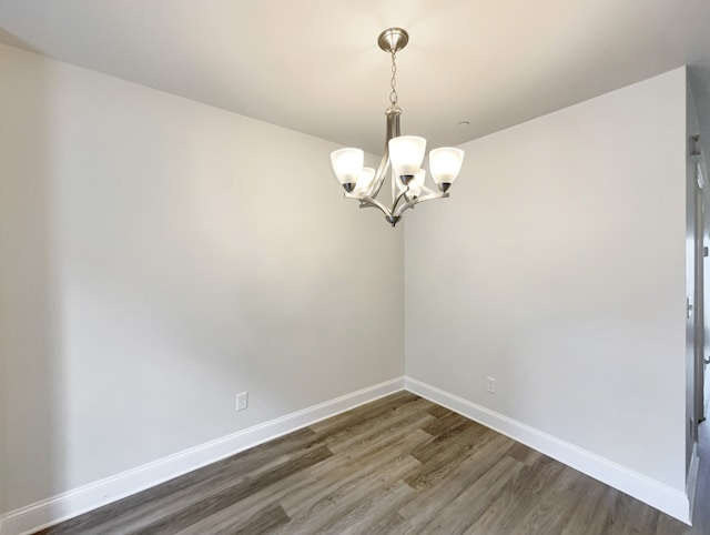 spare room with a chandelier and dark wood-type flooring