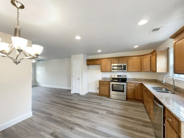 kitchen with pendant lighting, sink, appliances with stainless steel finishes, a notable chandelier, and light wood-type flooring