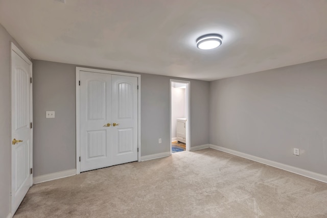 unfurnished bedroom with a closet, ensuite bathroom, and light carpet