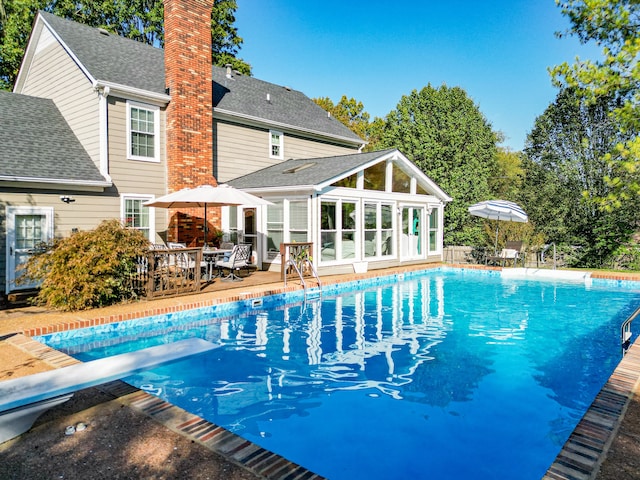 view of pool featuring a diving board, a sunroom, and a wooden deck