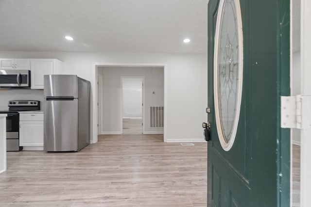 interior space featuring light wood-type flooring, appliances with stainless steel finishes, and white cabinets