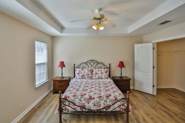 bedroom featuring hardwood / wood-style floors, ceiling fan, a closet, a tray ceiling, and a walk in closet