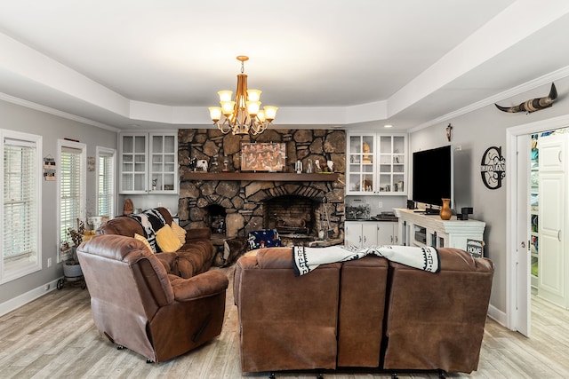 living room with crown molding, light hardwood / wood-style flooring, a stone fireplace, and a chandelier