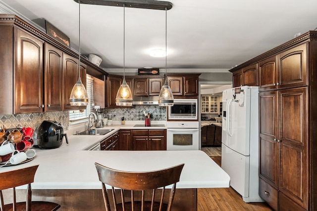 kitchen with a breakfast bar area, white appliances, pendant lighting, kitchen peninsula, and sink