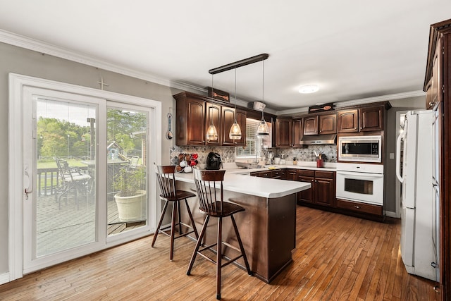 kitchen with white appliances, decorative light fixtures, a kitchen breakfast bar, kitchen peninsula, and light hardwood / wood-style floors