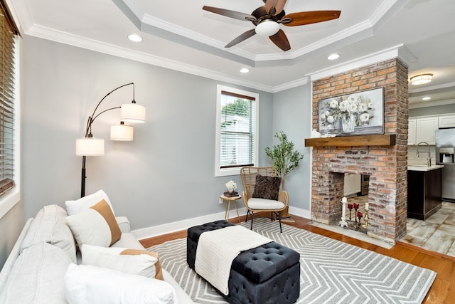 living room with a raised ceiling, light hardwood / wood-style flooring, ceiling fan, ornamental molding, and a fireplace