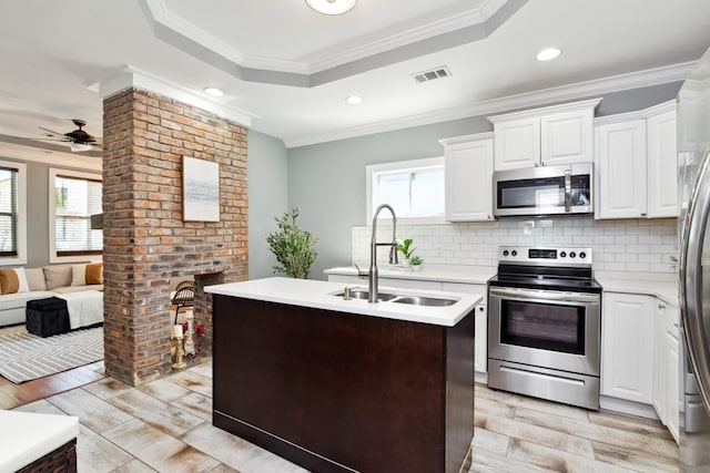 kitchen featuring a kitchen island with sink, sink, ornamental molding, a tray ceiling, and stainless steel appliances