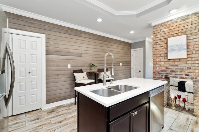 kitchen featuring stainless steel dishwasher, wood walls, sink, and an island with sink