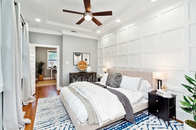 bedroom featuring ceiling fan, ornamental molding, dark wood-type flooring, and a tray ceiling