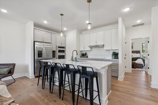 kitchen featuring appliances with stainless steel finishes, light hardwood / wood-style flooring, hanging light fixtures, and an island with sink