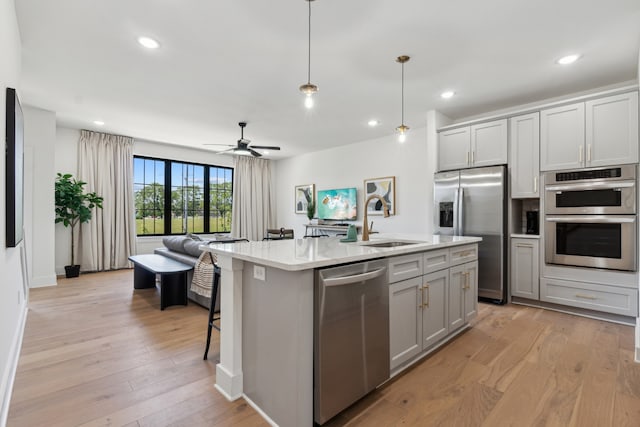 kitchen with a center island with sink, sink, hanging light fixtures, light hardwood / wood-style floors, and stainless steel appliances