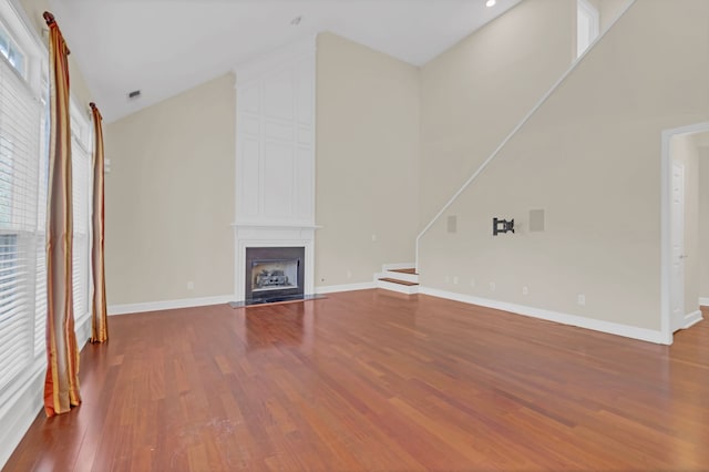 unfurnished living room with a large fireplace, high vaulted ceiling, and wood-type flooring