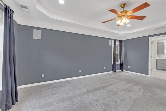 unfurnished bedroom with a raised ceiling, light colored carpet, ensuite bathroom, and ceiling fan