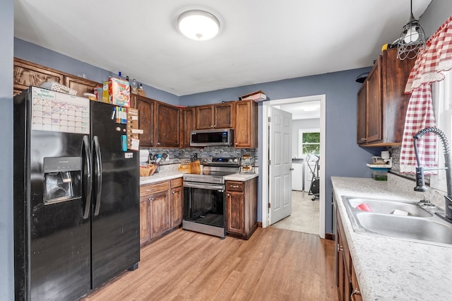 kitchen featuring backsplash, light wood-type flooring, decorative light fixtures, appliances with stainless steel finishes, and sink