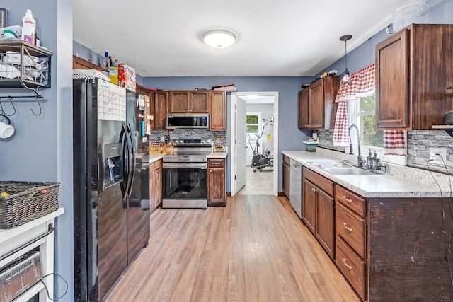 kitchen with light wood-type flooring, decorative light fixtures, appliances with stainless steel finishes, sink, and tasteful backsplash