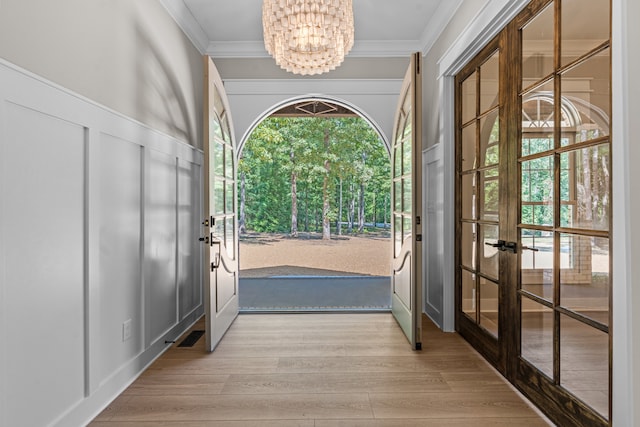 entryway featuring light wood-type flooring, french doors, a notable chandelier, and ornamental molding