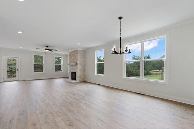 unfurnished living room with ceiling fan with notable chandelier, a fireplace, light hardwood / wood-style flooring, and a wealth of natural light