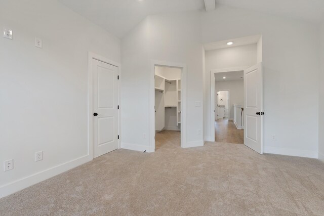 unfurnished bedroom with light carpet, a closet, lofted ceiling with beams, and a walk in closet