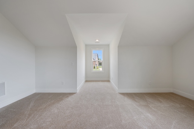 additional living space featuring vaulted ceiling and light colored carpet