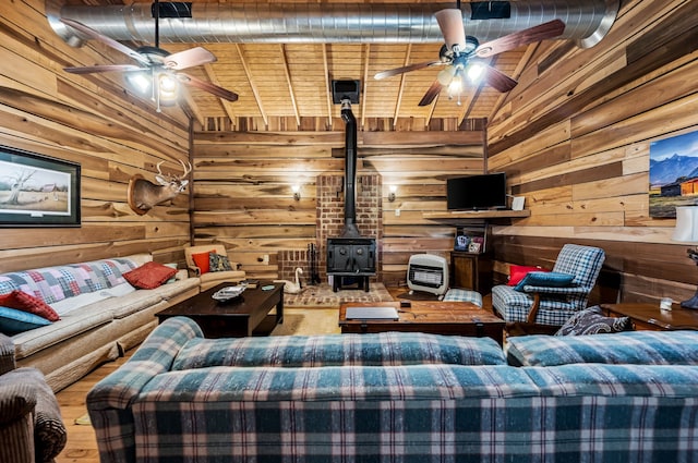 living room with wood walls, a wood stove, lofted ceiling, ceiling fan, and hardwood / wood-style flooring