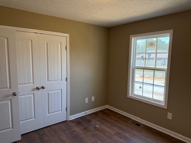 unfurnished bedroom with a closet, dark hardwood / wood-style flooring, and a textured ceiling