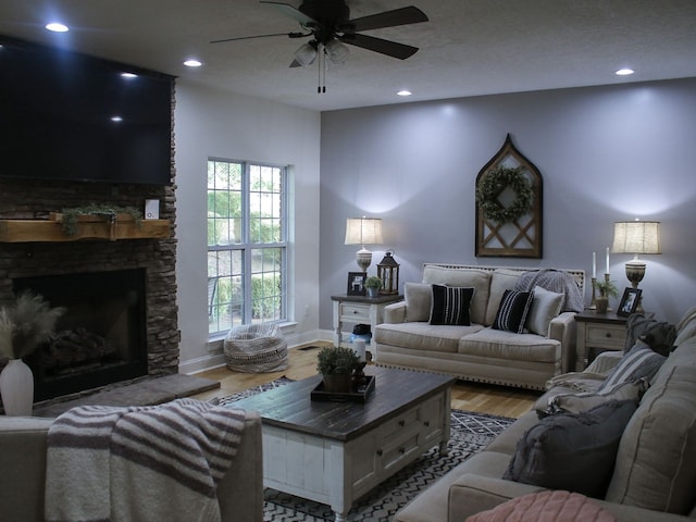 living room featuring light wood-type flooring, a textured ceiling, a stone fireplace, and ceiling fan