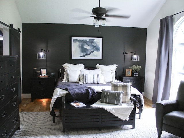 bedroom with a barn door, wood-type flooring, vaulted ceiling, and ceiling fan