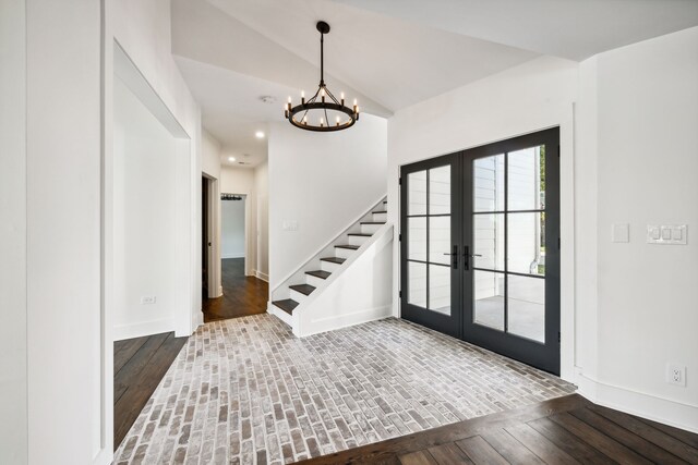 entrance foyer featuring hardwood / wood-style floors, an inviting chandelier, vaulted ceiling, and french doors