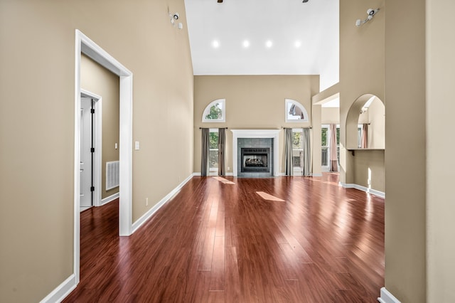 unfurnished living room with dark hardwood / wood-style floors, a towering ceiling, and a tiled fireplace