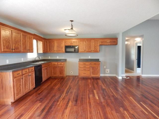 kitchen with pendant lighting, black appliances, dark wood-type flooring, and sink