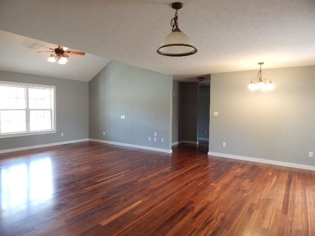 spare room with a textured ceiling, ceiling fan with notable chandelier, vaulted ceiling, and dark wood-type flooring