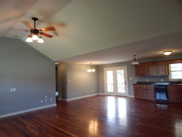 unfurnished living room with ceiling fan with notable chandelier, lofted ceiling, dark wood-type flooring, and sink