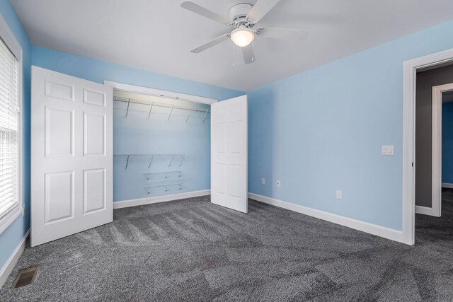 unfurnished bedroom featuring dark colored carpet, a closet, and ceiling fan