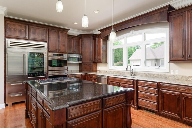 kitchen with light hardwood / wood-style floors, sink, a kitchen island, stainless steel appliances, and dark stone countertops