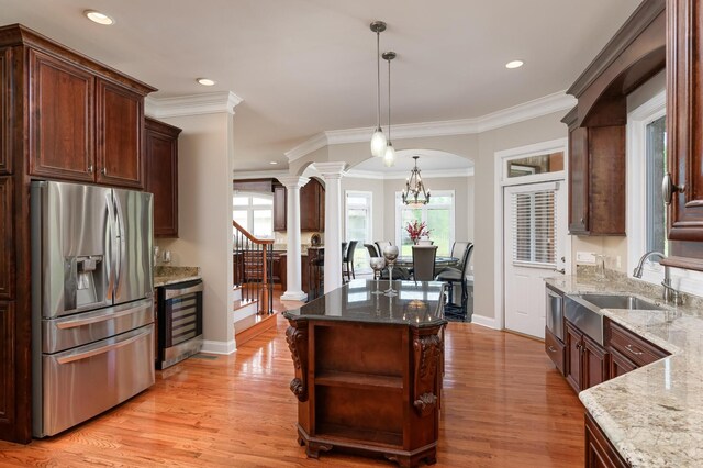 kitchen with light hardwood / wood-style floors, light stone counters, decorative light fixtures, stainless steel refrigerator with ice dispenser, and decorative columns