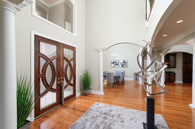 entryway with wood-type flooring, a high ceiling, a chandelier, and ornate columns