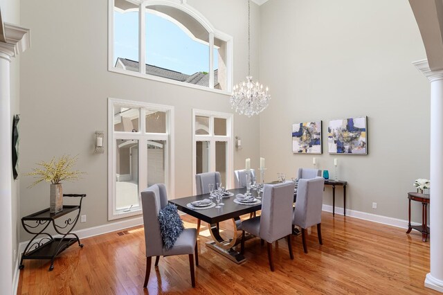 dining room with decorative columns, a towering ceiling, hardwood / wood-style floors, and a chandelier