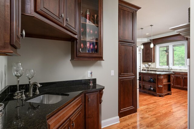 kitchen featuring dark stone counters, pendant lighting, sink, light hardwood / wood-style flooring, and crown molding