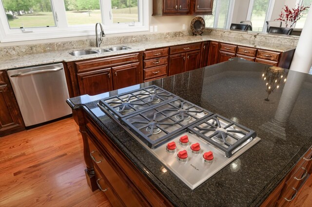 kitchen with appliances with stainless steel finishes, sink, dark stone counters, and light hardwood / wood-style flooring