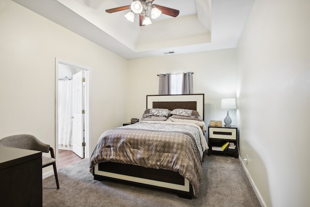 carpeted bedroom with ensuite bath, a tray ceiling, and ceiling fan