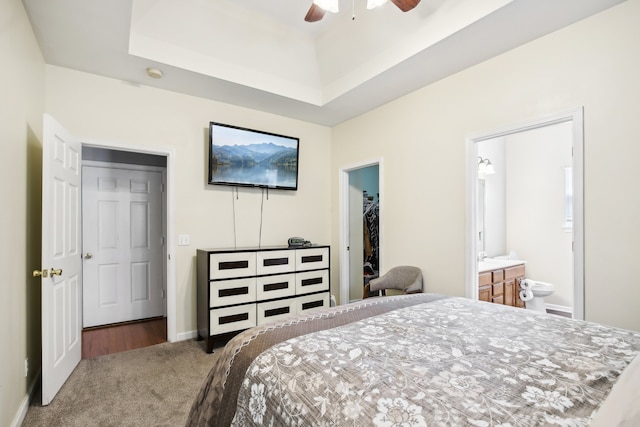 bedroom with carpet, ceiling fan, a tray ceiling, ensuite bathroom, and a walk in closet