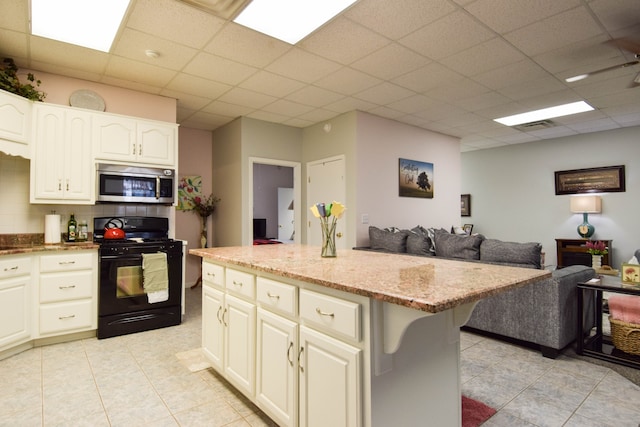 kitchen with light stone counters, a center island, a drop ceiling, light tile patterned floors, and black range with gas cooktop