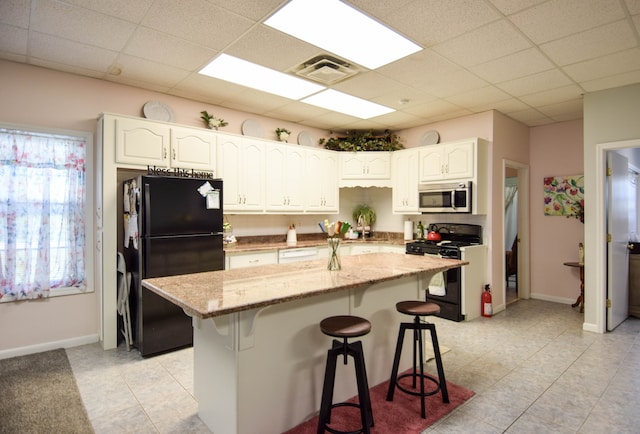 kitchen featuring white cabinets, a kitchen island, a breakfast bar, and black appliances