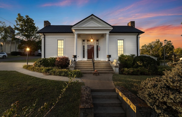 view of front facade with a chimney, metal roof, and a front lawn