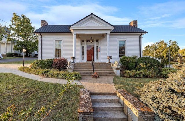 view of front facade featuring a front yard, metal roof, and a chimney