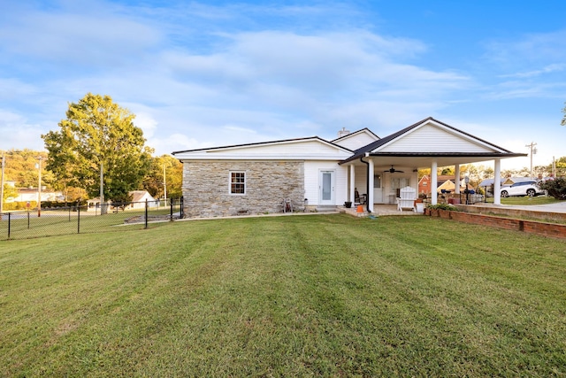 rear view of property with stone siding, a patio area, ceiling fan, a yard, and fence
